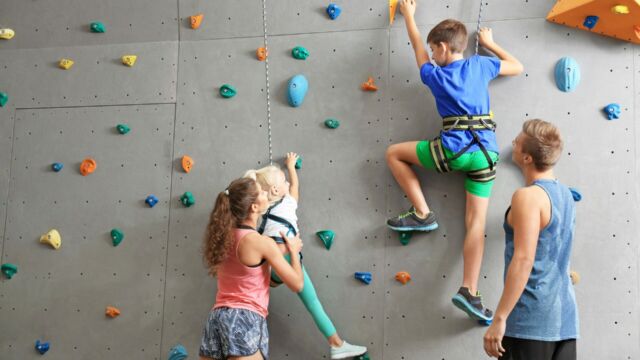 Instructors,helping,children,climb,wall,in,gym